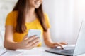 Happy young asian woman in yellow shirt using smartphone and laptop Royalty Free Stock Photo