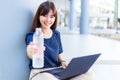 Happy young attractive Asian woman smiling and holding out the bottle of water to the camera while working on her laptop computer Royalty Free Stock Photo