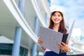 Happy young attractive female Asian engineer wearing hard hat holding her large size blueprint folder while standing outside of Royalty Free Stock Photo