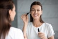 Happy attractive woman applying mascara on eyelashes looking in mirror Royalty Free Stock Photo