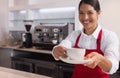 Happy young barista offering cup of coffee smiling at camera Royalty Free Stock Photo