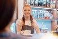 Happy young barista offering cup of coffee while smiling at camera or to her client, wearing white casual t shirt and brown apron Royalty Free Stock Photo