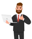 Happy young bearded business man holding/showing a latest new laptop and gesturing/making thumbs up sign with hand fingers. Like. Royalty Free Stock Photo