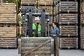 Happy young bearded guy driver in helmet in forklift truck with box full green apples