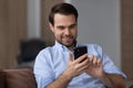 Happy young bearded guy sit on sofa enjoy using phone