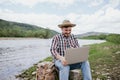 Happy Young bearded man in hat sits on stone and works on laptop, remote work concept