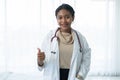 Happy young beautiful African American female doctor in white medical coat with stethoscope standing with thumbs up and smiling on Royalty Free Stock Photo