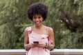 Happy young beautiful afro american woman smiling and using mobile phone. Green background. Spring or summer season. Casual Royalty Free Stock Photo