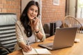 Happy young beautiful Asian business woman taking on the phone while using a computer during working from her home office Royalty Free Stock Photo