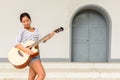 Happy young beautiful Asian woman playing guitar outdoors Royalty Free Stock Photo