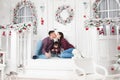 Happy young beautiful caucasian family mother and father kissing with child sitting on white porch of merry christmas decoration Royalty Free Stock Photo