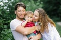 Happy young beautiful family with a young son is enjoying a wonderful day in a summer park. Young parents kiss a child Royalty Free Stock Photo
