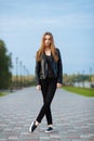 Happy young beautiful woman in black leather jacket black jeans slip-on posing for model tests in the summer park Royalty Free Stock Photo