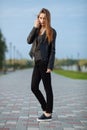 Happy young beautiful woman in black leather jacket black jeans slip-on posing for model tests in the summer park Royalty Free Stock Photo