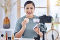 Happy young beauty blogger holding up a beauty product and sponge while doing a make-up tutorial and recording with her