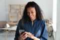 Happy young biracial business woman holding smartphone, looking at screen.