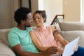 Happy young biracial couple using laptop while sitting together on sofa at home Royalty Free Stock Photo