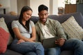 Happy young biracial couple in casual clothing sitting on sofa using digital tablet at home Royalty Free Stock Photo