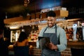 Happy young biracial man in apron using digital tablet while working as waiter in restaurant Royalty Free Stock Photo