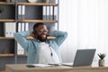 Happy young black bearded man in glasses and headphones rejoices in successful deal, relax and looks at laptop Royalty Free Stock Photo