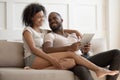 Happy young black couple using digital tablet sit on sofa