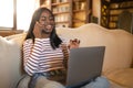 Online work, education concept. Happy young black lady having phone conversation, using laptop computer at home Royalty Free Stock Photo