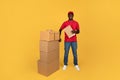 Happy young black man courier in red uniform with clipboard in warehouse, cheks many boxes Royalty Free Stock Photo