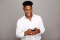 Happy young black man looking at mobile phone by gray wall Royalty Free Stock Photo