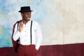 Happy young black man with suspenders and hat smiling by wall Royalty Free Stock Photo