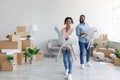 Happy young black man and woman carry chairs in new home with boxes. Couple placing furniture, moving to new flat Royalty Free Stock Photo
