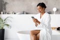 Happy young black woman in bathrobe browsing her smartphone Royalty Free Stock Photo