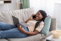 Happy black woman laying on couch with laptop and smartphone Royalty Free Stock Photo