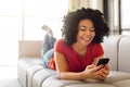 Happy young black woman messaging on smartphone while relaxing at home Royalty Free Stock Photo