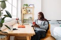 Happy young black woman in muslim headscarf using smartphone at home