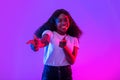 Happy young black woman pointing fingers at camera, choosing you, smiling in neon light Royalty Free Stock Photo