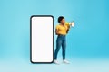 Happy young black woman shouting into megaphone, standing near giant smartphone with blank screen, mockup for design Royalty Free Stock Photo