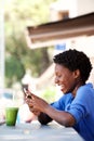 Happy young black woman sitting at cafe reading text message on cell phone Royalty Free Stock Photo