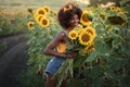 Happy young black woman walks in the sunflower field. Smiling dark-skinned girl with with a bouquet of sunflowers and Royalty Free Stock Photo