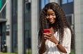 Happy young black woman using mobile phone standing outdoors. Royalty Free Stock Photo