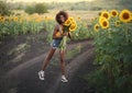 Happy young black woman walks in the sunflower field. Smiling dark-skinned girl with with a bouquet of sunflowers and Royalty Free Stock Photo