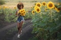 Happy young black woman walks in the sunflower field. Smiling dark-skinned girl with with a bouquet of sunflowers and Royalty Free Stock Photo