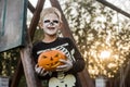 Happy young blond hair boy with skeleton costume holding jack o lantern. Halloween. Trick or treat. Outdoors portrait