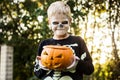 Happy young blond hair boy with skeleton costume holding jack o lantern. Halloween. Trick or treat. Outdoors portrait