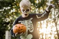 Happy young blond hair boy with skeleton costume holding jack o lantern. Halloween. Trick or treat. Outdoors portrait