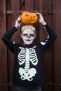 Happy young blond hair boy with skeleton costume holding jack o lantern. Halloween. Trick or treat. Outdoors portrait over wooden Royalty Free Stock Photo