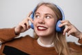 Happy young blonde female with bright red lips enjoying favorite song while listening it on headphones. Using earphones Royalty Free Stock Photo