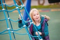 A happy young blonde girl on a blue rope ladder in a playground Royalty Free Stock Photo