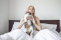 Happy young blonde hair 20s woman with grey unhappy cat lying in a white bed at home in the morning. Pets, comfort, rest Royalty Free Stock Photo