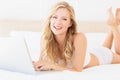 Happy young blonde lying on her bed using laptop Royalty Free Stock Photo