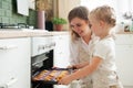 Happy young blonde mom and little daughter get ready-made cookies from the oven at home. A happy family. Cooking with children Royalty Free Stock Photo